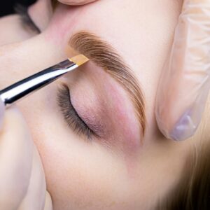 the eyebrow lamination master holds the model's eyebrow and applies a toning cream to redness