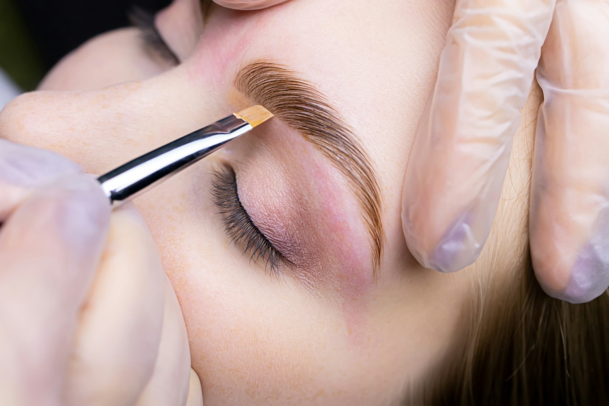 the eyebrow lamination master holds the model's eyebrow and applies a toning cream to redness